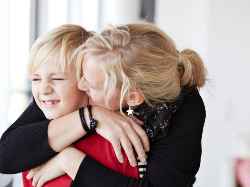 Mutter küsst ihren jungen Sohn, der peinlich wegschaut.