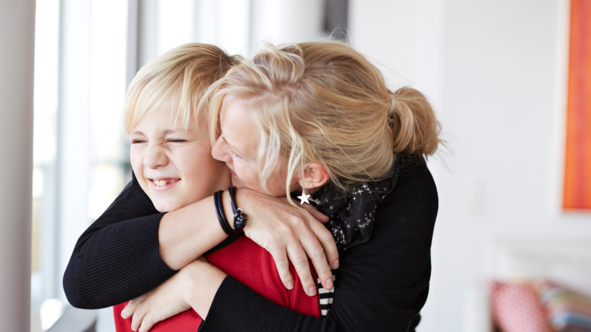 Mutter küsst ihren jungen Sohn, der peinlich wegschaut.