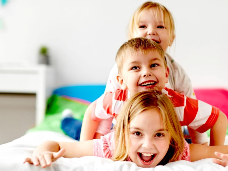 Drei Geschwisterkinder liegen übereinander 'gestapelt' auf dem Bett.