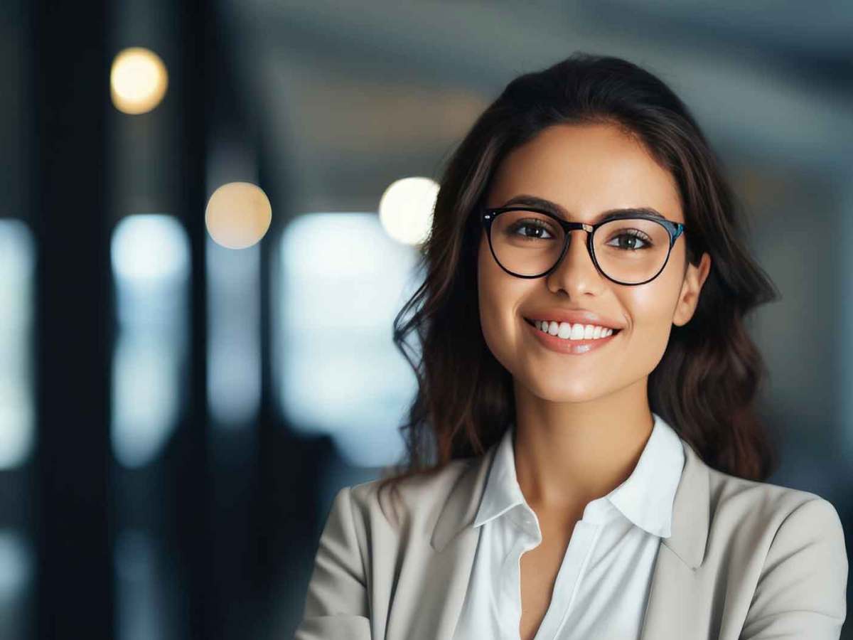 Junge, selbstbewusste Frau mit Brille und braunen Haaren lächelt.