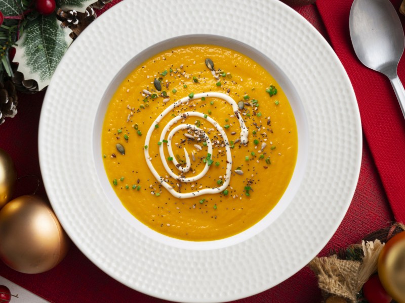 Cremige Karottensuppe in weißem Teller auf weihnachtlich gedeckten Tisch.