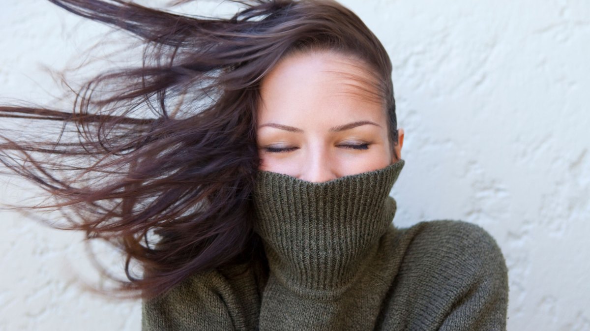 Frau mit einem Rollkragenpullover in dem sie ihr Gesicht versteckt