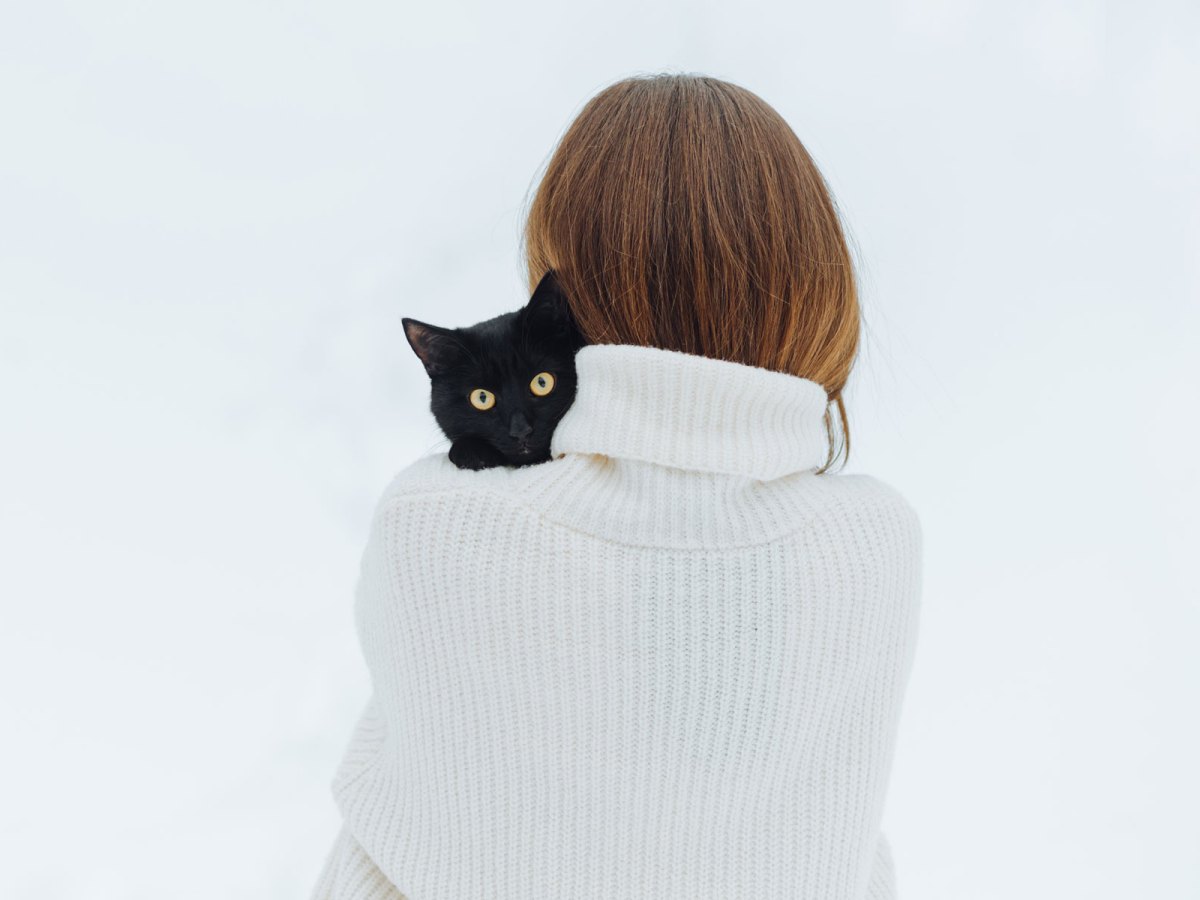 Frau mit einem weißen Pullover und einer schwarzen Katze auf dem Arm