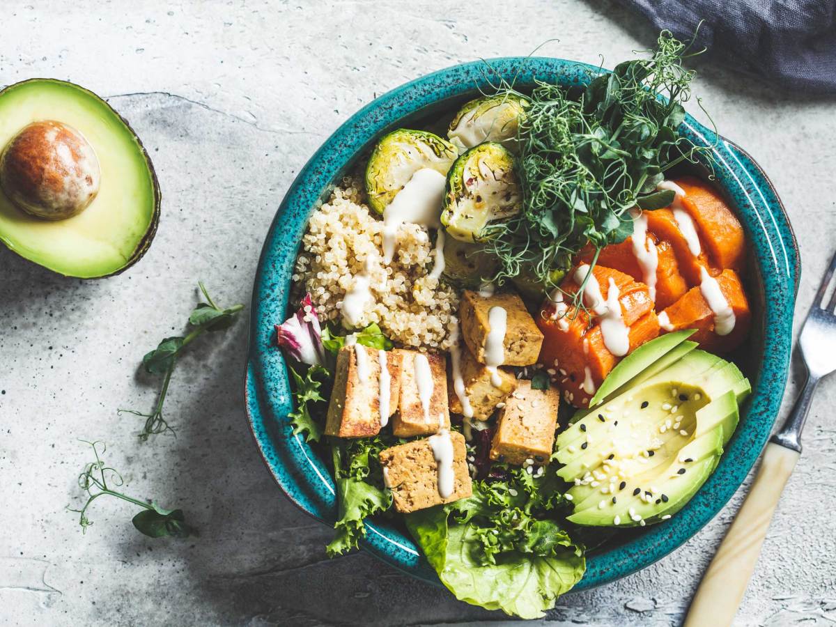 Buddha-Bowl mit Quinoa, Tofu, Avocado, Süßkartoffel, Rosenkohl und Tahini-Dressing, Ansicht von oben. Gesundes veganes Essenskonzept.