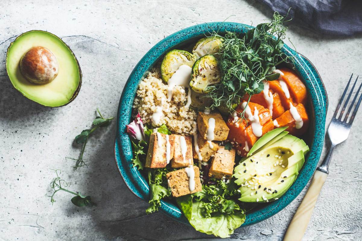 Buddha-Bowl mit Quinoa, Tofu, Avocado, Süßkartoffel, Rosenkohl und Tahini-Dressing, Ansicht von oben. Gesundes veganes Essenskonzept.