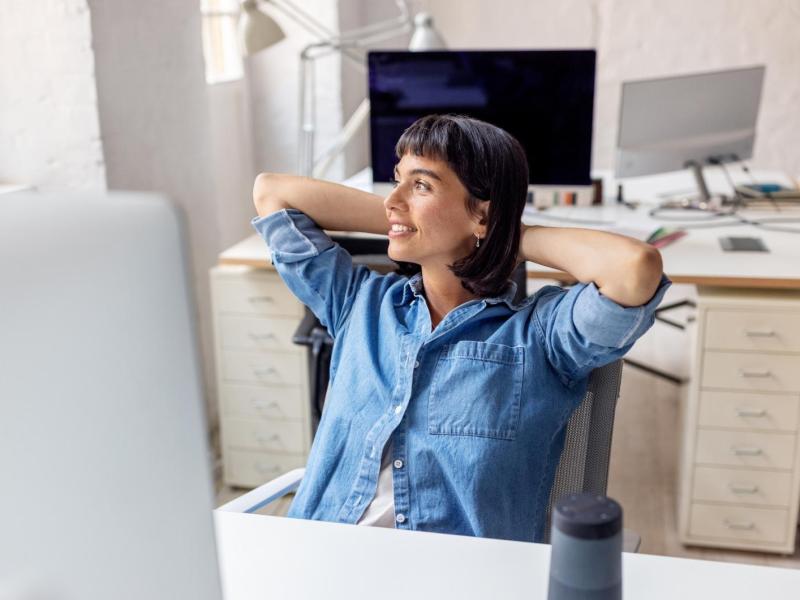 Frau lehnt sich auf dem Bürostuhl zurück und guckt aus dem Fenster.