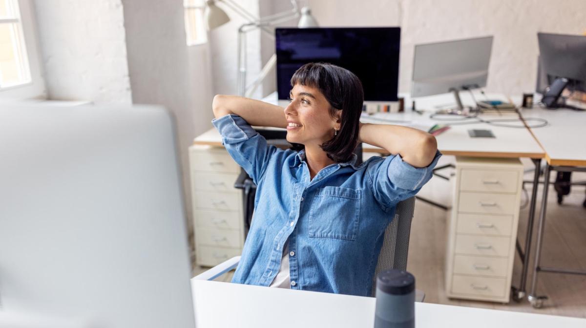 Frau lehnt sich auf dem Bürostuhl zurück und guckt aus dem Fenster.