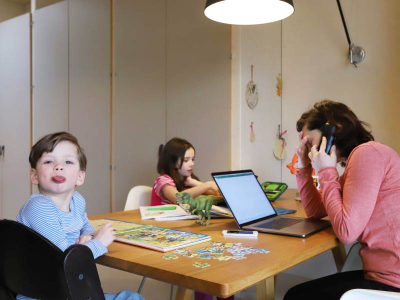 Mutter versucht aus dem Homeoffice zu arbeiten, während ihre Kinder ebenfalls am Tisch sitzen und spielen.