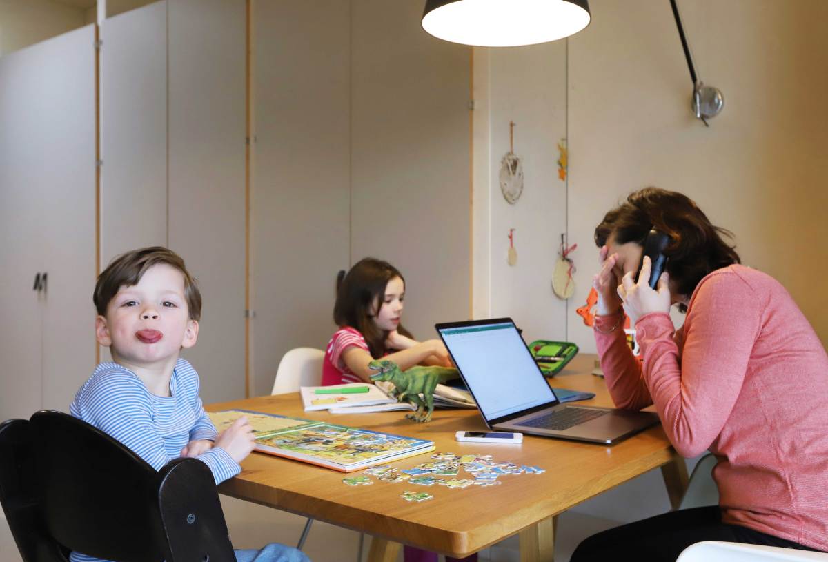 Mutter versucht aus dem Homeoffice zu arbeiten, während ihre Kinder ebenfalls am Tisch sitzen und spielen.