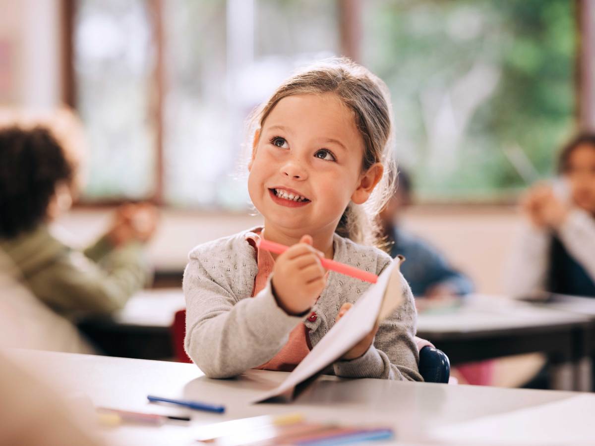 Schulanfängerin sitzt in der Klasse und zeigt etwas auf ihrem Block.