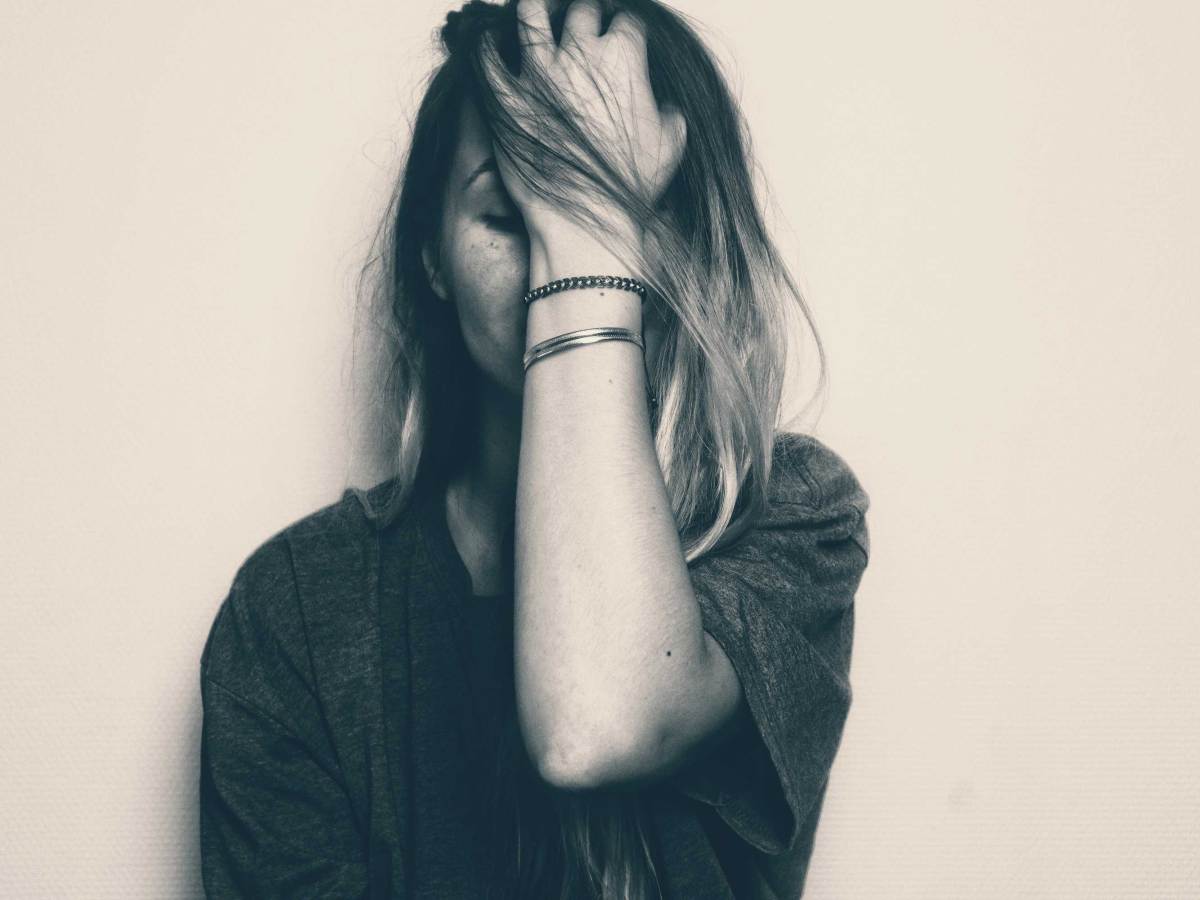 Blondes M&auml;dchen bedeckt ihr Gesicht mit der linken Hand. Bild in schwarz-wei&szlig;. Darstellung von traurigen, besorgten, frustrierten Emotionen