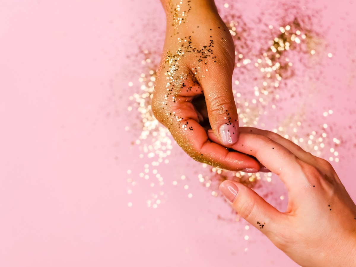 Zwei H&auml;nde mit GLitzer vor rosa Hintergrund, die sich an den Fingerspitzen ber&uuml;hren und anfassen