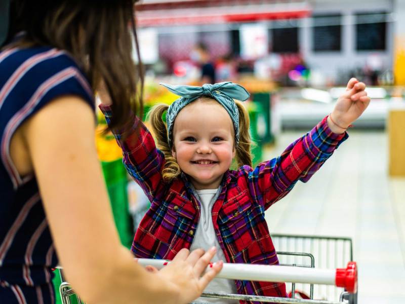 Mutter schiebt ihre Tochter im Einkaufswagen durch den Supermarkt.