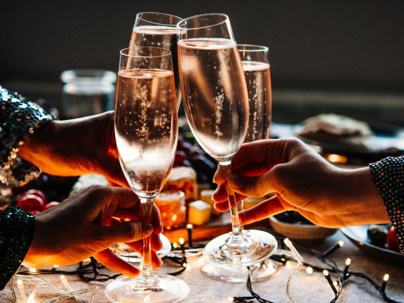 Nahaufnahme von Händen mit je einem Sektglas, die anstoßen.