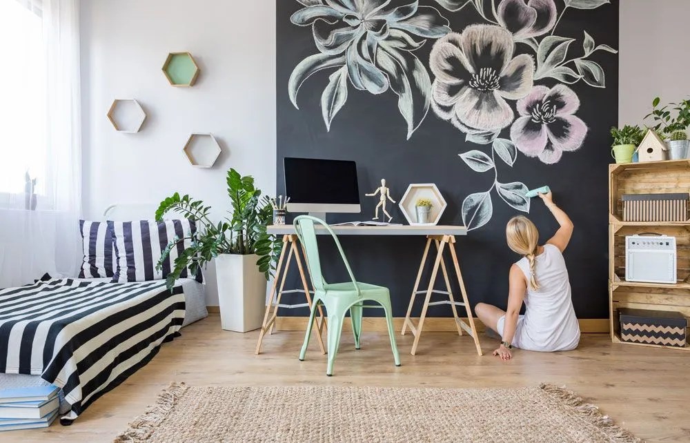 Frau auf einem Boden im Wohnzimmer, die die Wand mit einem Pinsel mit Blumen bemalt