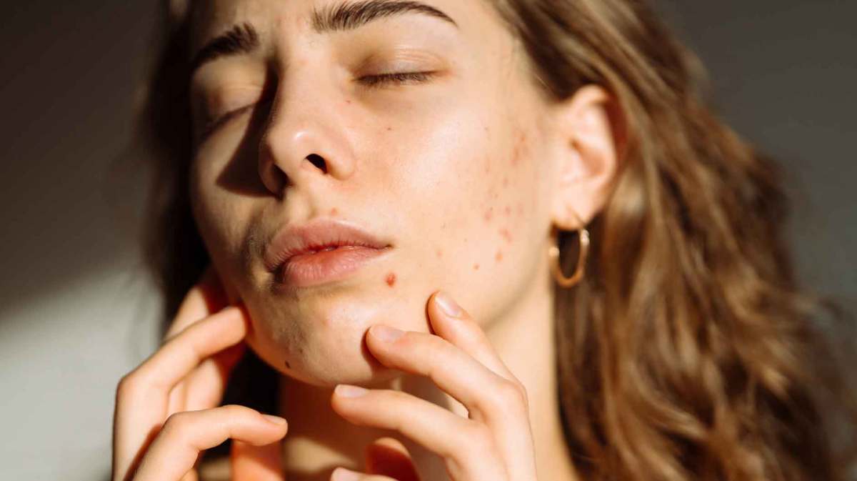 Frau berührt ihr Gesicht mit ihren Händen und steht im Sonnenlicht.