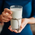 Junge Frau hält ein Glas Milch in der Hand.