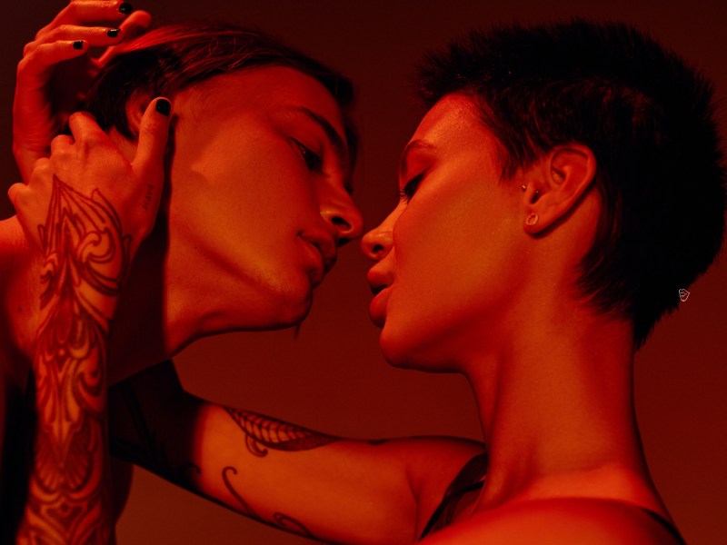 Frau und Mann in rotem Licht, die sich leidenschaftlich ansehen und kurz davor sind, sich zu küssen.