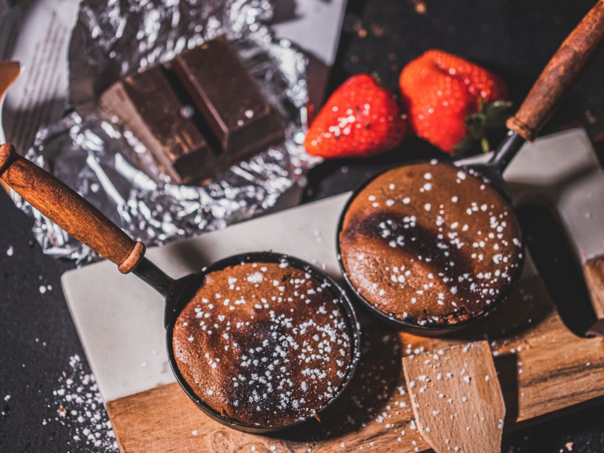 Raclette Pf&auml;nnchen auf Holztisch, die mit Schokokuchen gef&uuml;llt sind.