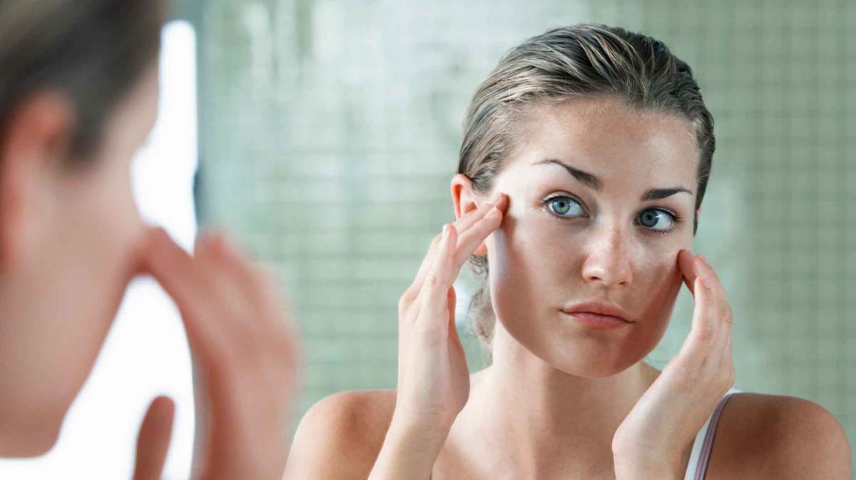 Frau cremt sich vor dem Spiegel das Gesicht mit Feuchtigkeitscreme ein.