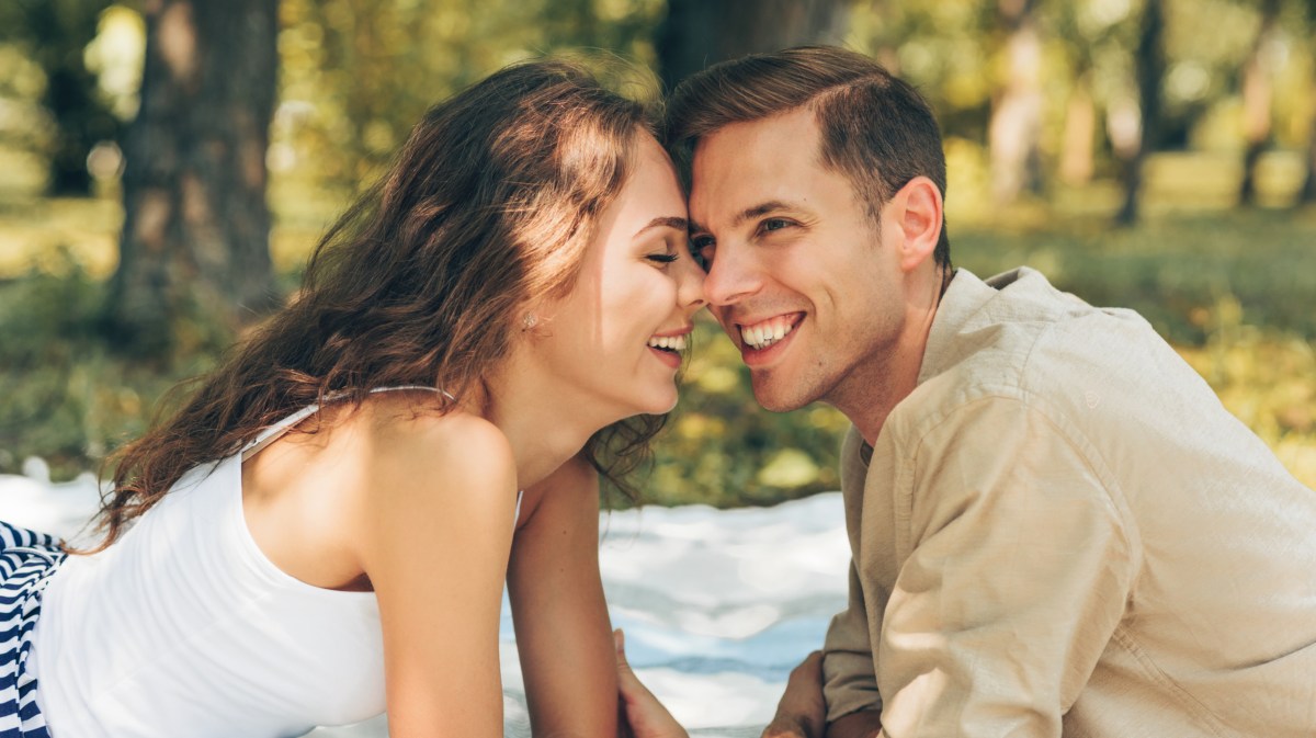 Frau und Mann im Park auf einer Decke im Sommer, die sich anlächeln