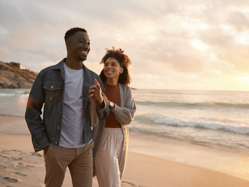 Mann und Frau am Strand, die gemeinsam am Strand im Sonnenuntergang entlang laufen