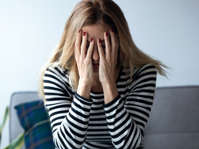 Frau, die auf dem Sofa sitzt und ihre Hände verzweifelt vor das Gesicht hält