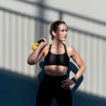 Krafttraining Frauen: Trainierte Frau in Sport-BH und Leggings mit gelber Kettlebell vor Wand