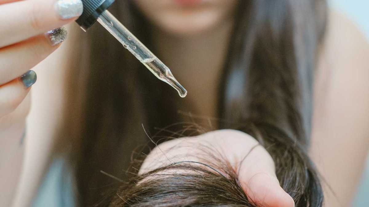 Frau trägt mit einer Pipette Öl auf die Haare auf