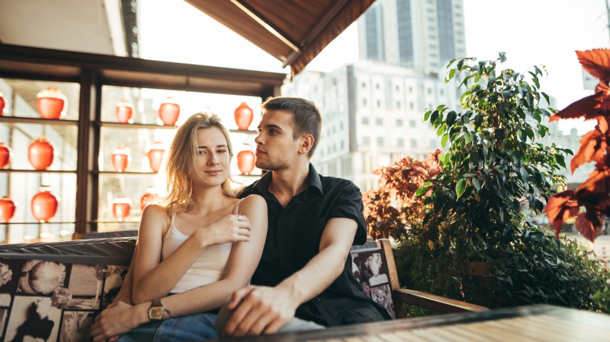 Mann und Frau in Café, die in der Sonne draußen sitzen und sich umarmen