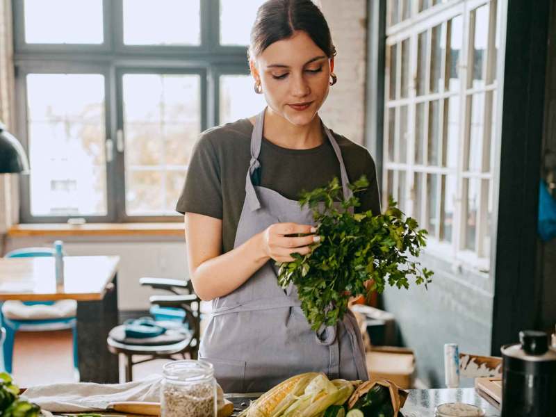 Eine Frau kocht in ihrer Küche und zupft Kräuter.