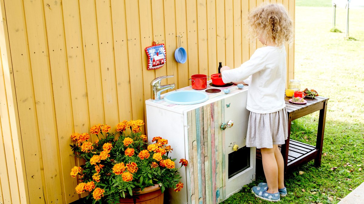 Kleines Mädchen spielt draußen mit ihrer Matschküche.