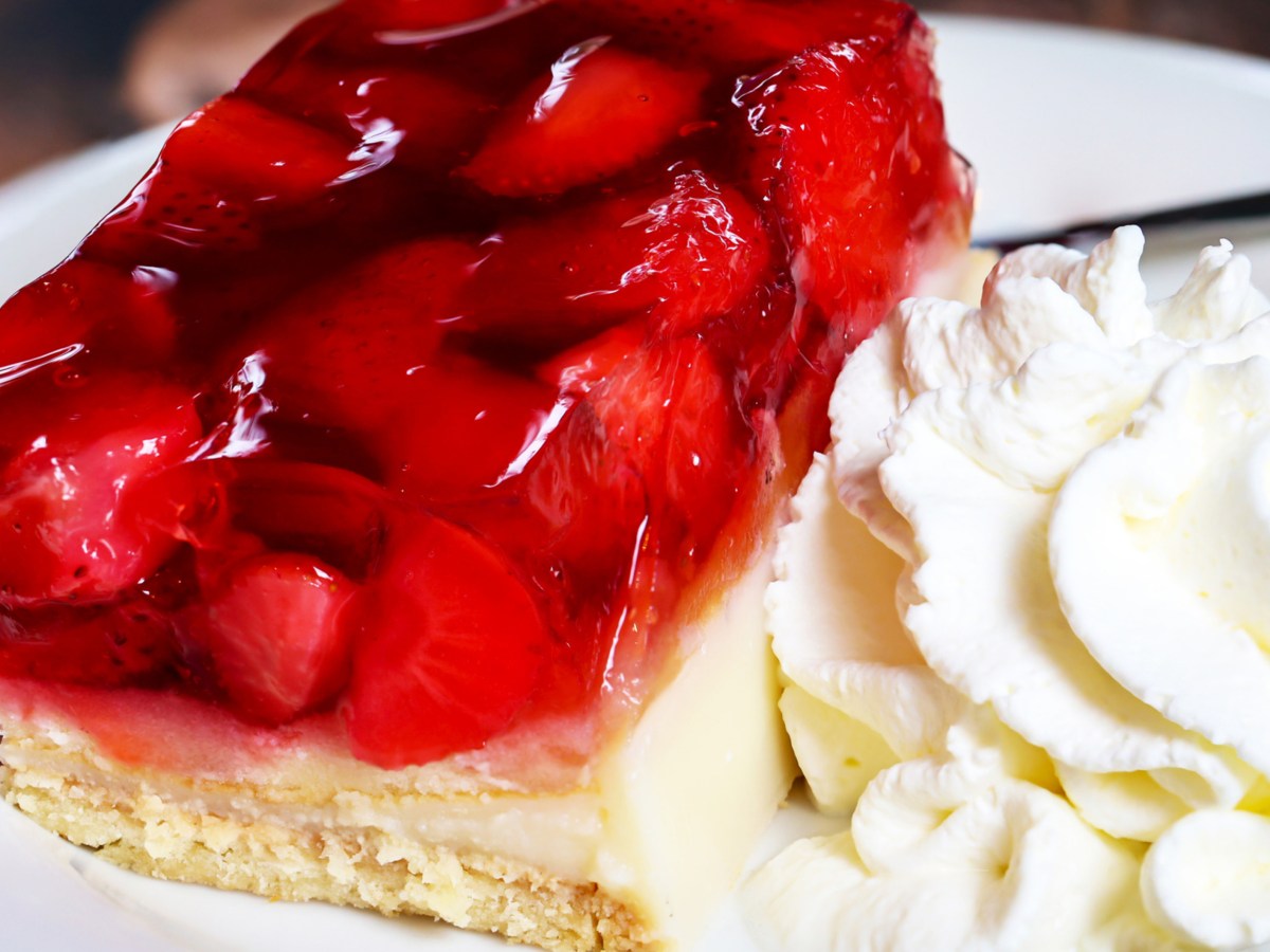 Erdbeerkuchen-Schnitte mit Sahne auf weißem Teller.