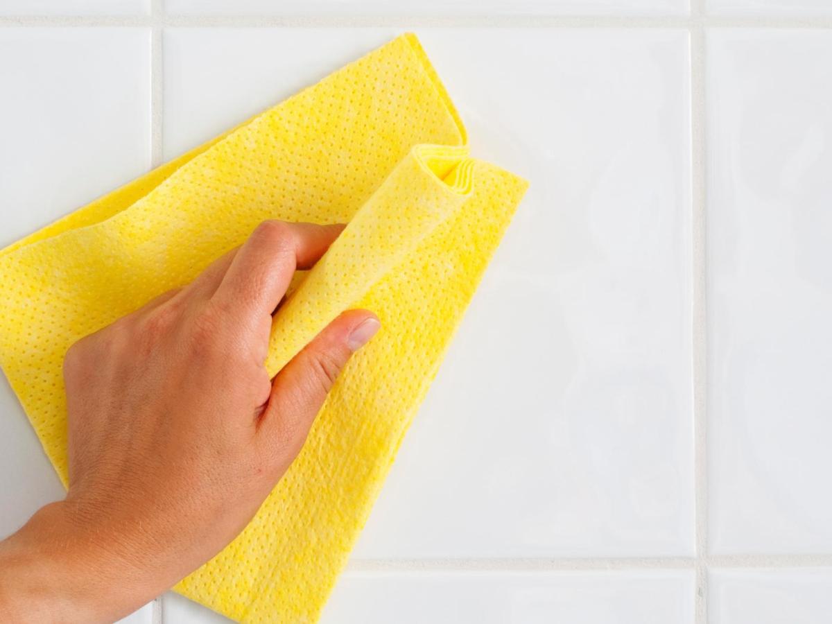 Frau reinigt die Fliesen mit einem gelben Tuch.