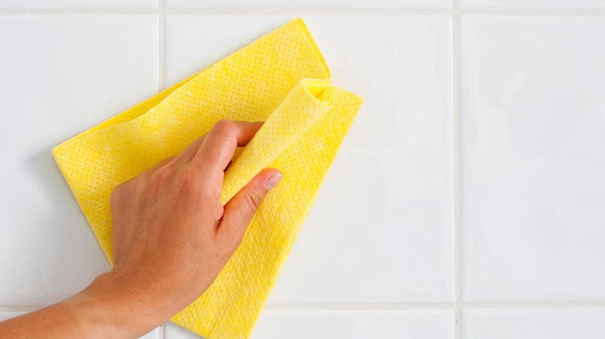 Frau reinigt die Fliesen mit einem gelben Tuch.