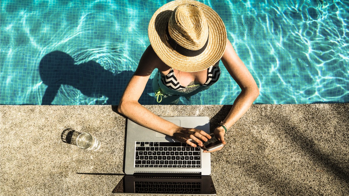 Frau mit Sonnenhut und Laptop am Pool