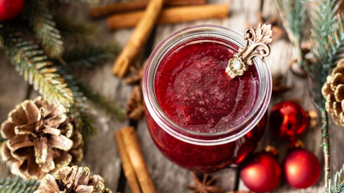 Rotes Fruchtgelee auf Holztisch mit Tannenzapfen daneben.