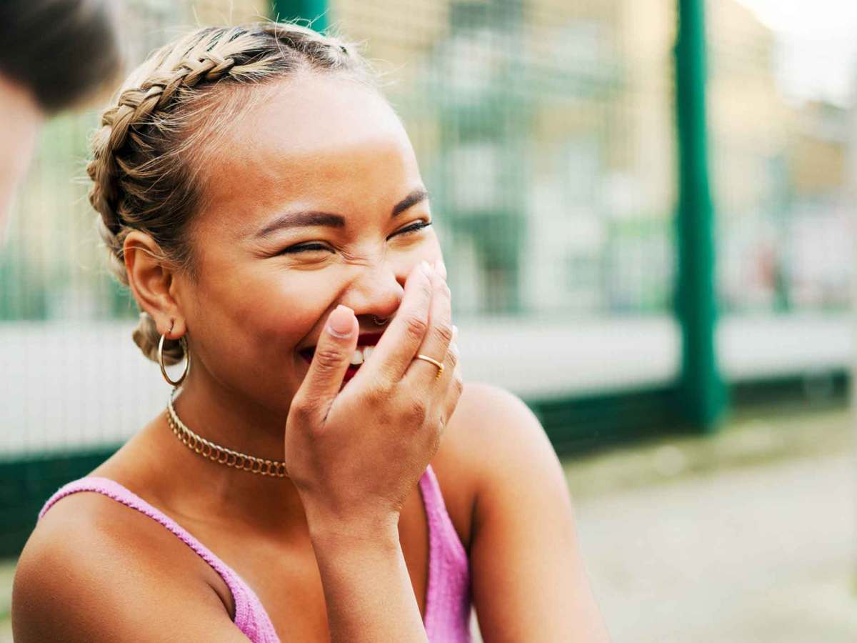 Junge Frau mit einem rosa Top lacht und h&auml;lt sich die Hand vor den Mund.