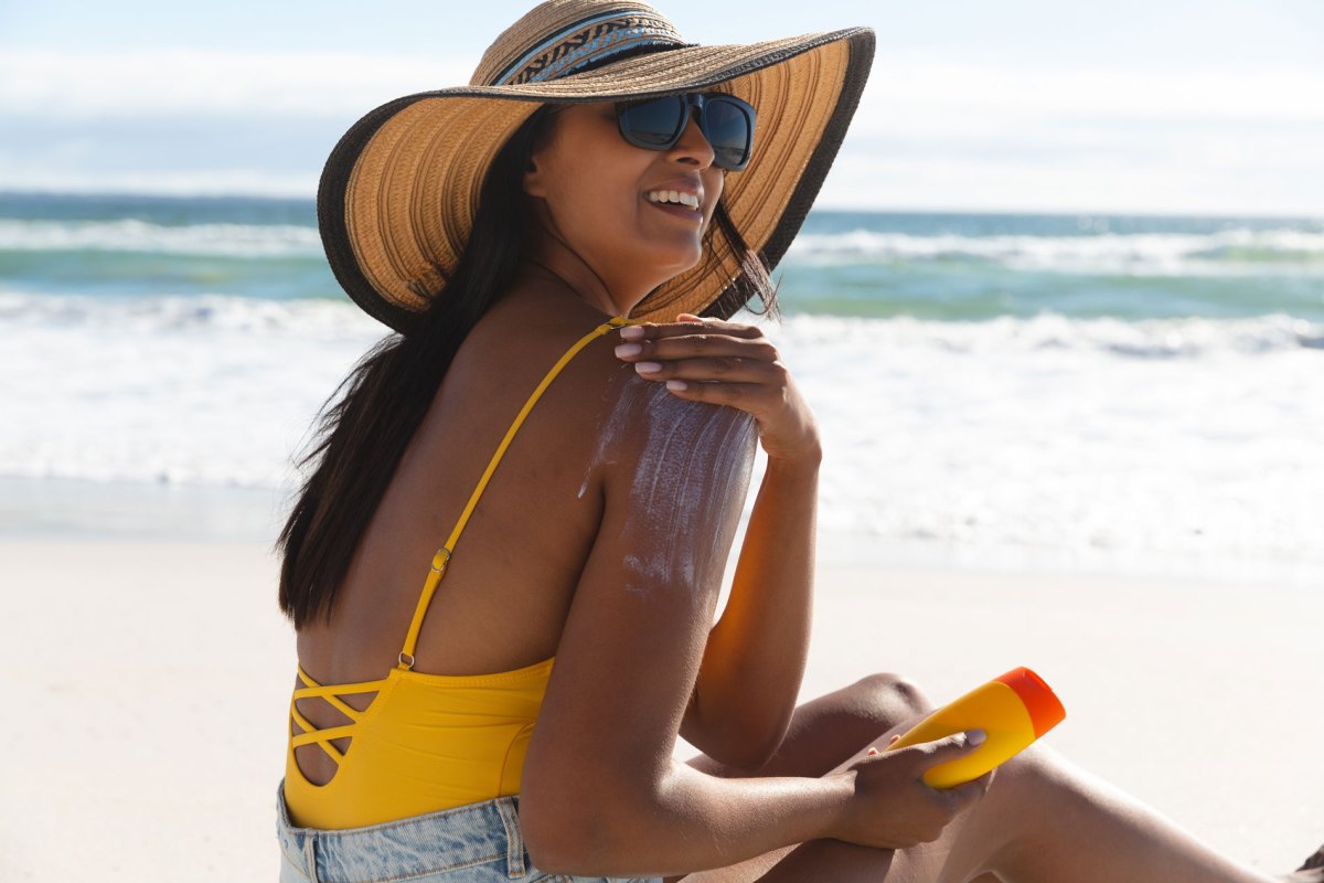 Frau beim Auftragen von Sonnencreme am Strand.