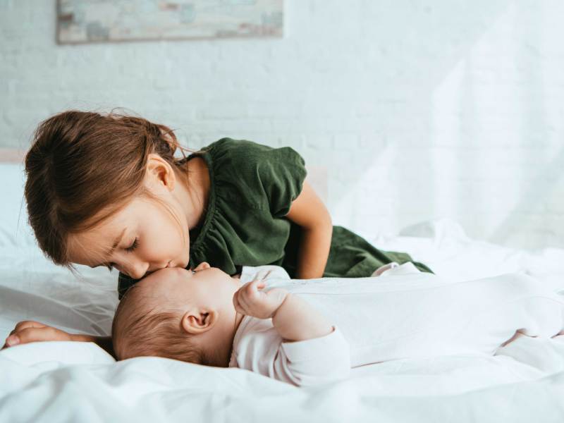 Große Schwester gibt ihrer kleinen Babyschwester einen Kuss auf die Stirn.