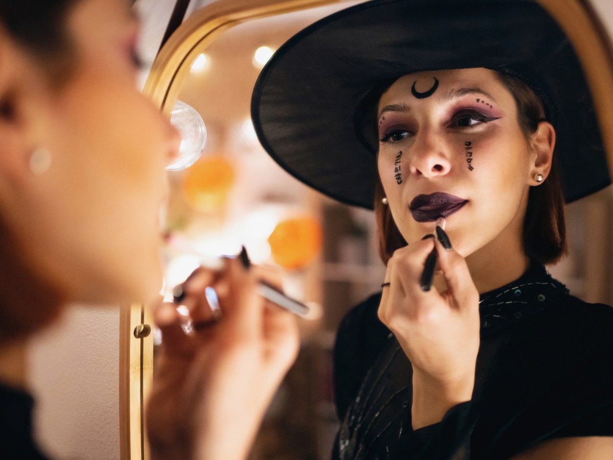 Frau schmint sich als Hexe zu Halloween.