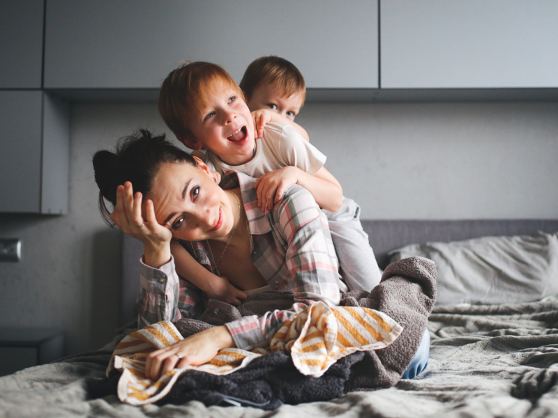 Müde Mutter mit zwei Kindern auf dem Rücken und Wäsche auf dem Tisch vor ihr