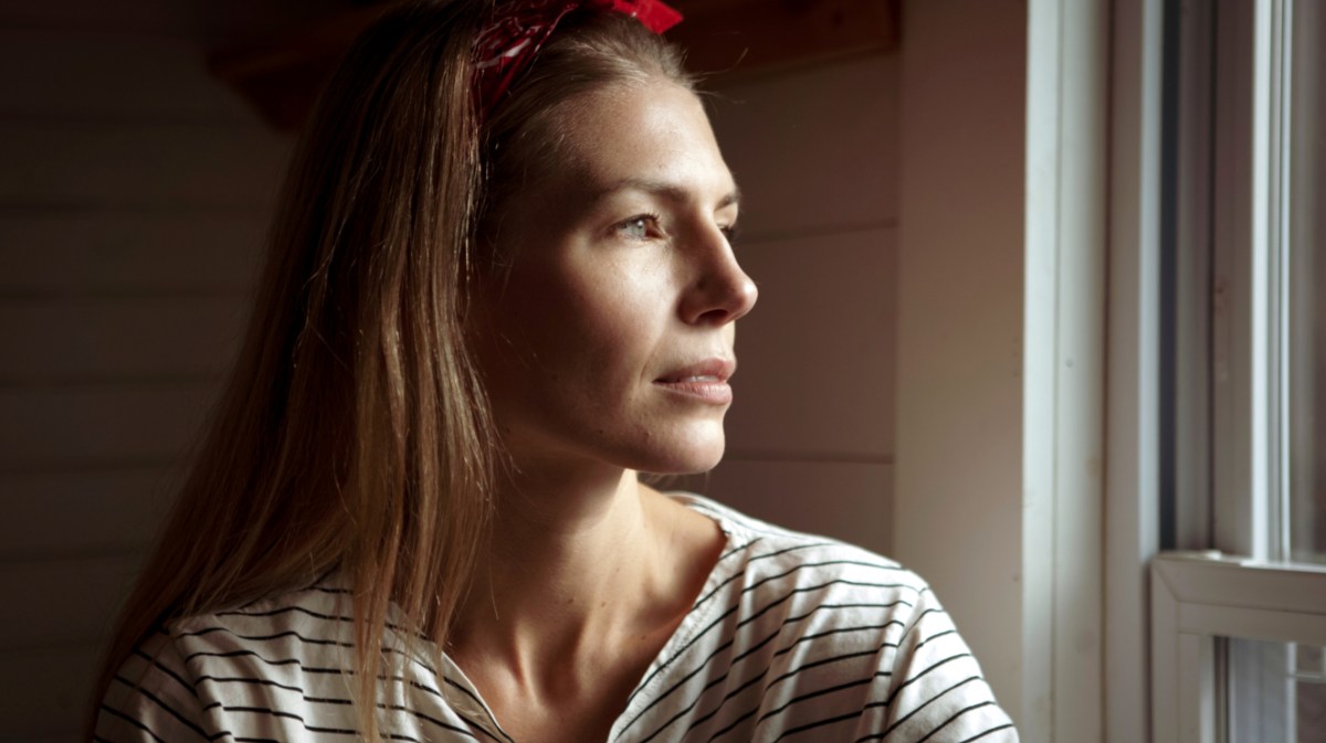 Frau schaut nachdenklich aus dem Fenster.