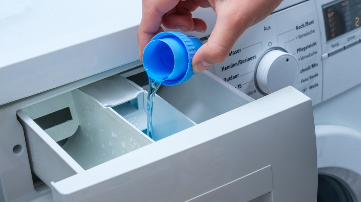 Person füllt flüssiges Waschmittel in Waschmaschinenfach.