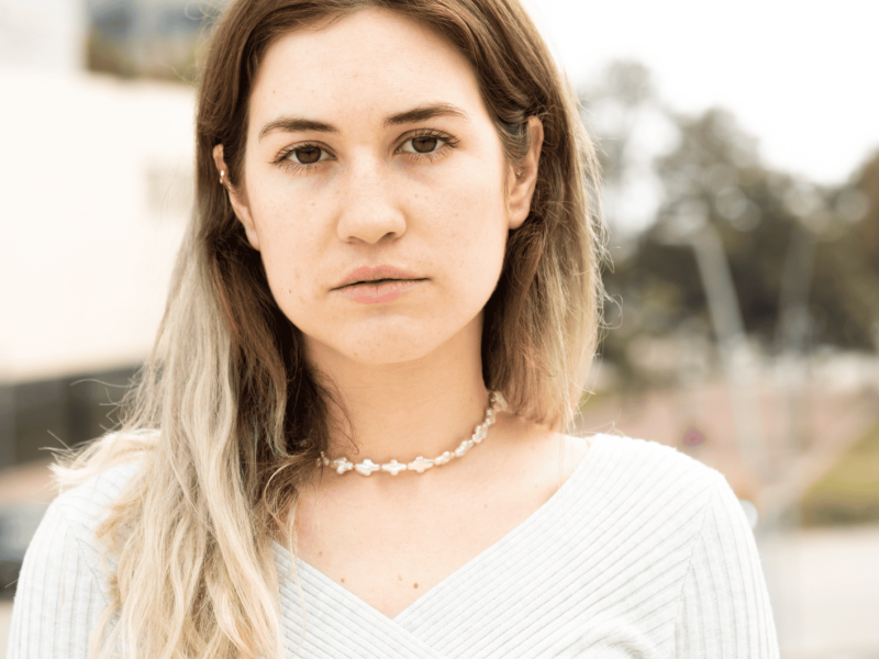 Junge Frau mit braunen Haaren und Perlenkette schaut ernst