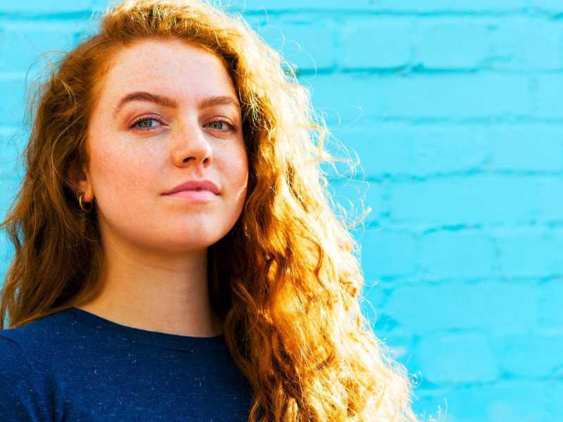 Portrait einer Frau neben einer hellblauen Wand.