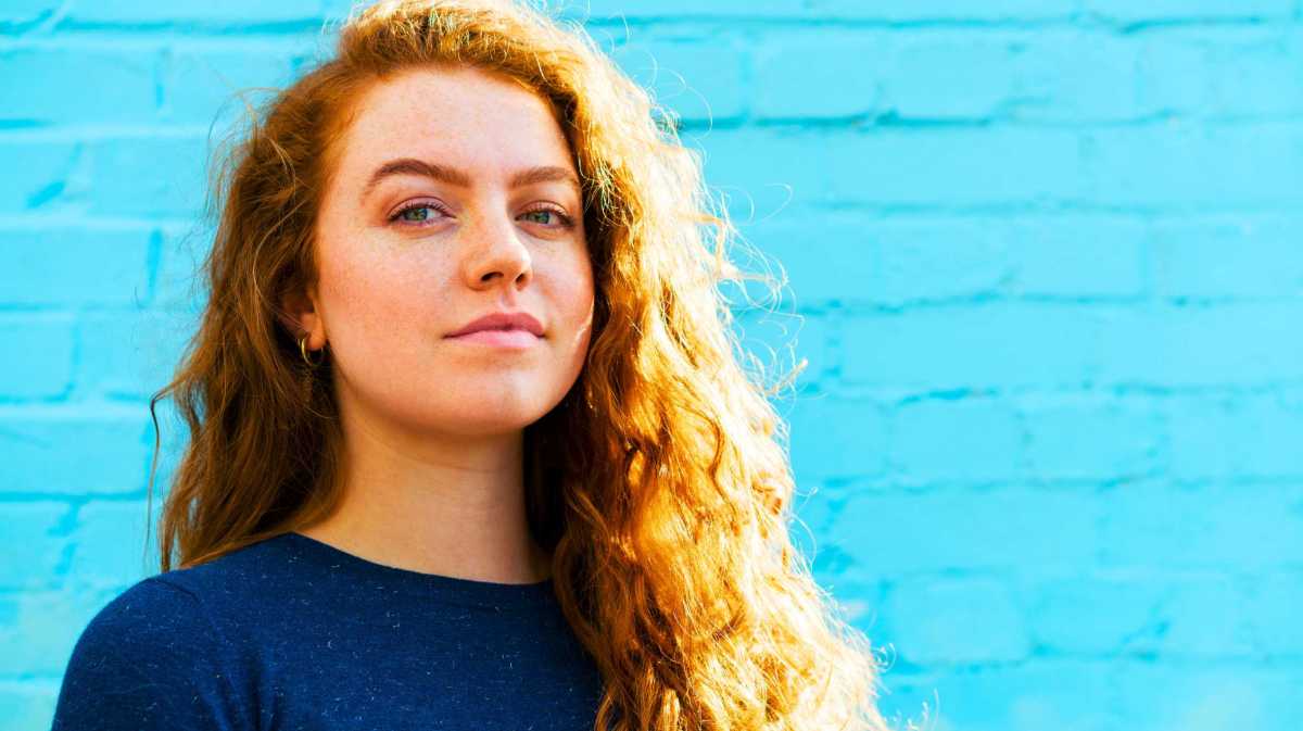 Portrait einer Frau neben einer hellblauen Wand.