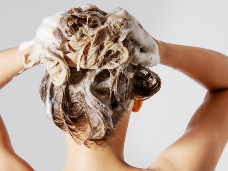 Frau mit Rücken zur Kamera, shamponiert ihre Haare ein.