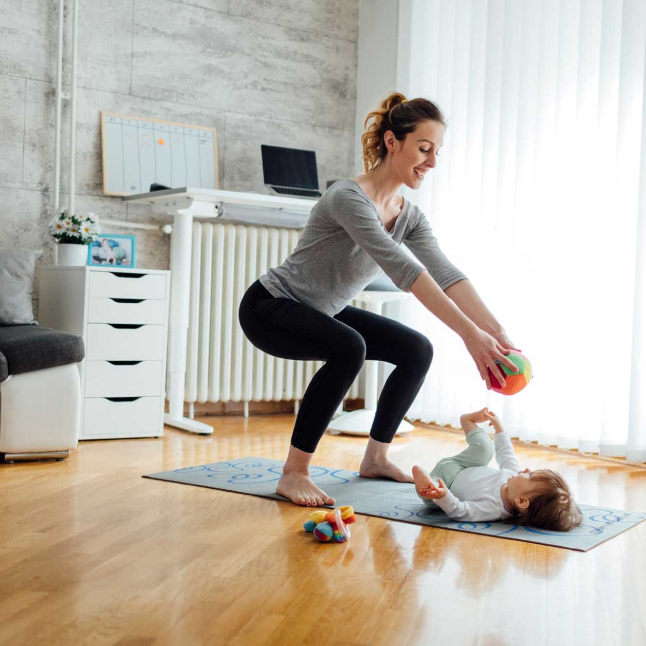 Mutter macht eine Kniebeuge und zeigt ihrem Baby einen Ball