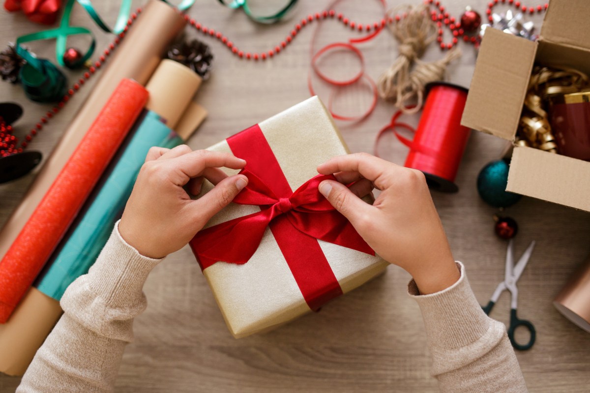 Eine Frau verpackt ein Geschenk in Geschenkpapier und bindet eine Schleife darum.